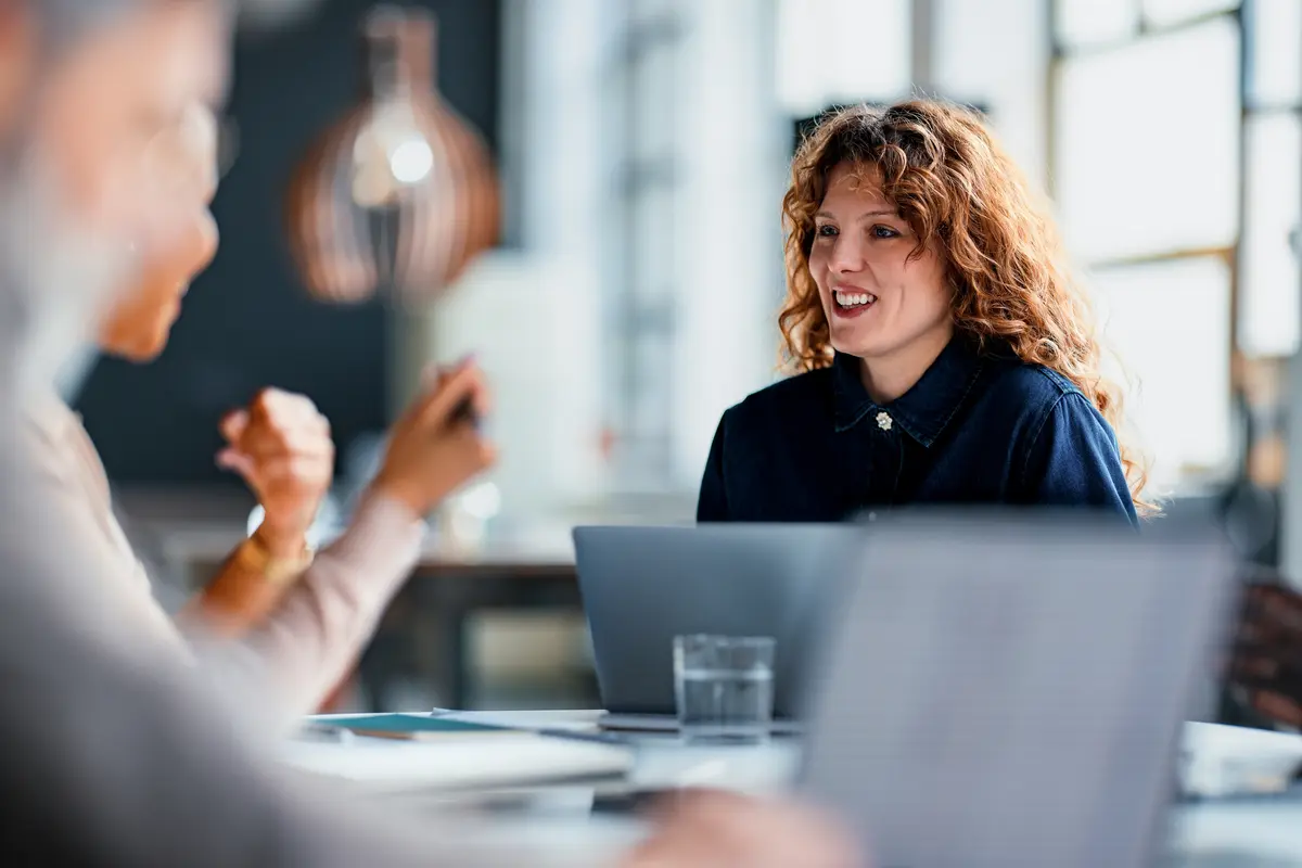 A woman smiling and talking with colleagues across a meeting table